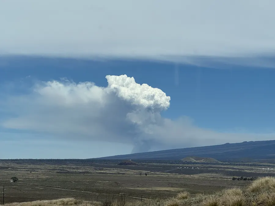 A distant eruption plume rising over the volcanic landscape