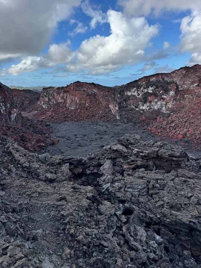 Pāhoehoe lava pooled in a small crater with oxidized red walls at Fissure 8