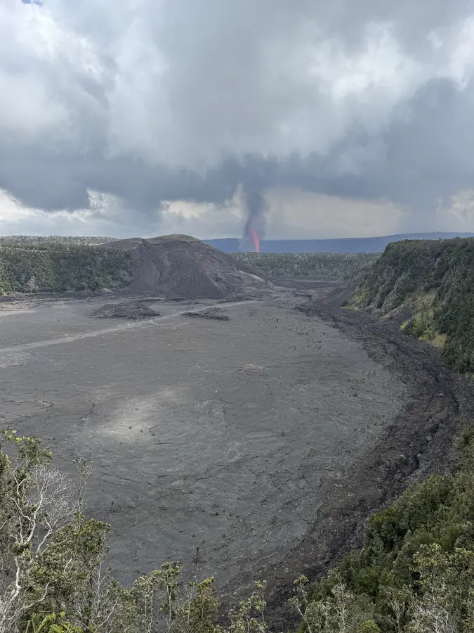 Kīlauea Iki crater floor with an eruption plume rising in the distance