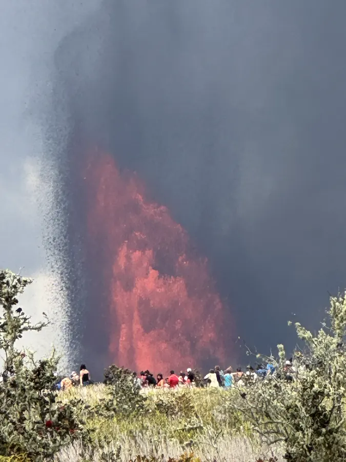 Onlookers watching a glowing lava fountain at dusk